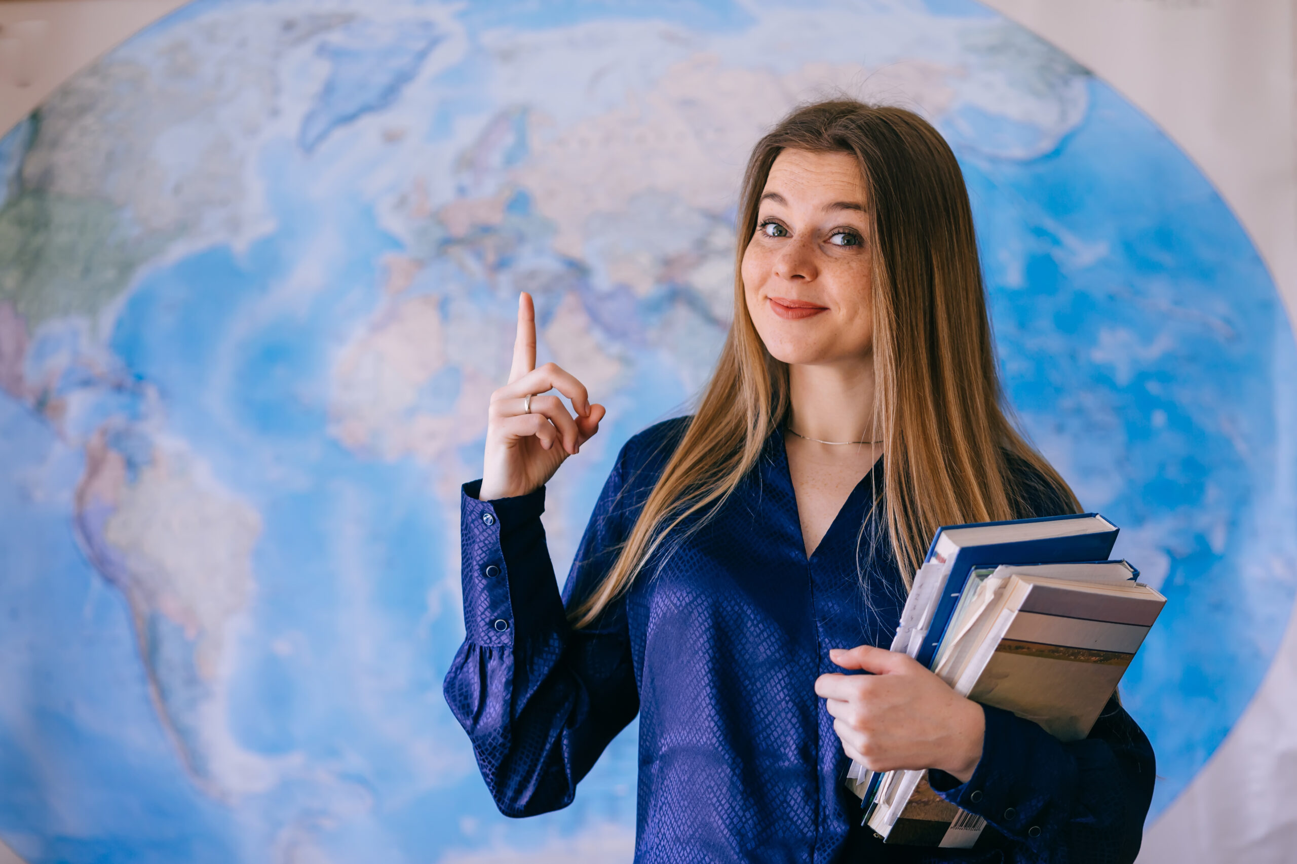 Young woman holding books over world map background point with finger. Global education concept.